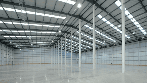 Modern pre-engineered steel building interior with spacious warehouse floor, steel columns, roofing panels, skylights and industrial lighting.